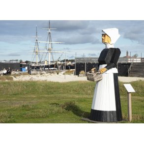 Trskulptur af kvinde ved stranden i Ebeltoft og med Fregatten Jylland i baggrunden
