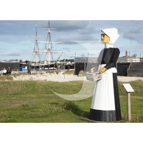 Trskulptur af kvinde ved stranden i Ebeltoft og med Fregatten Jylland i baggrunden